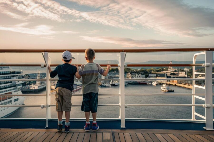 Two kids standing side by side, dressed casually, on cruise ship with Greenock in the background
