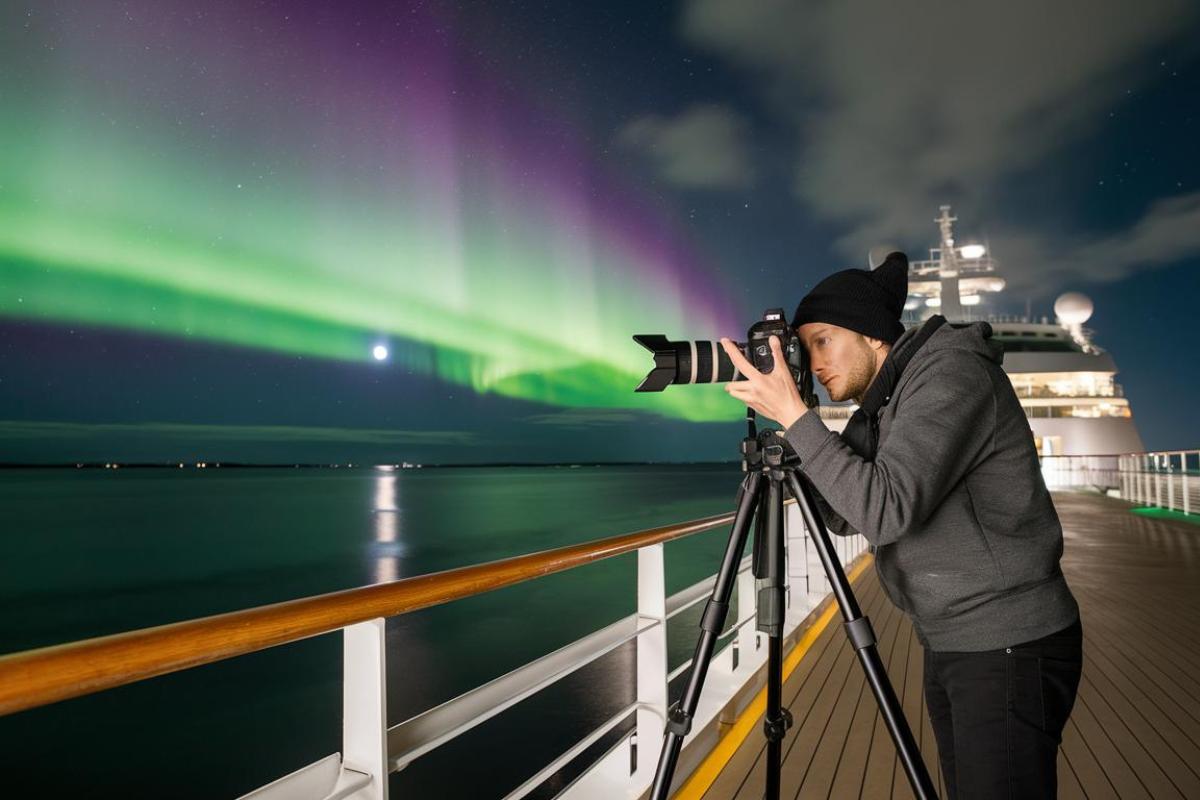 Person taking a photo of the northern lights from a cruise ship with a camera on a tripod