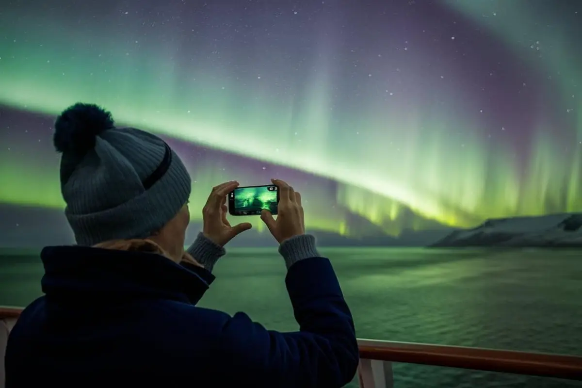 Person taking a photo of the northern lights from a cruise ship with a mobile phone