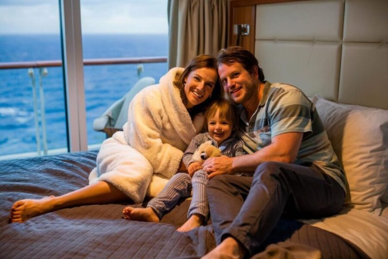 Mom and Dad with baby sitting on their bed on a family cruise ship