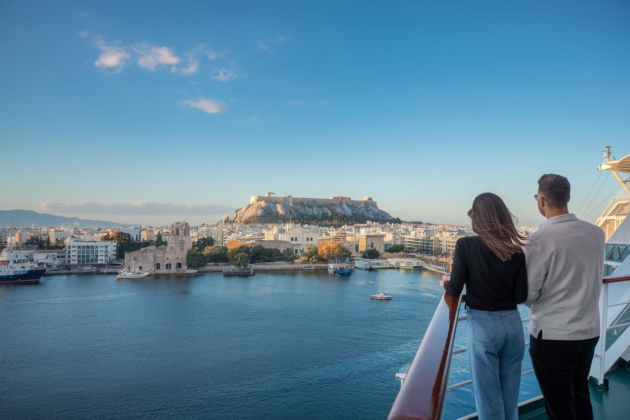 2 guests. dressed casually. looking out to the city. on a cruise ship with Athens, Greece in the background