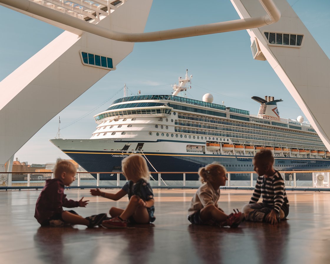 kids sitting on the floor playing. There is a cruise ship in the background on a sunny day at Port of Dover