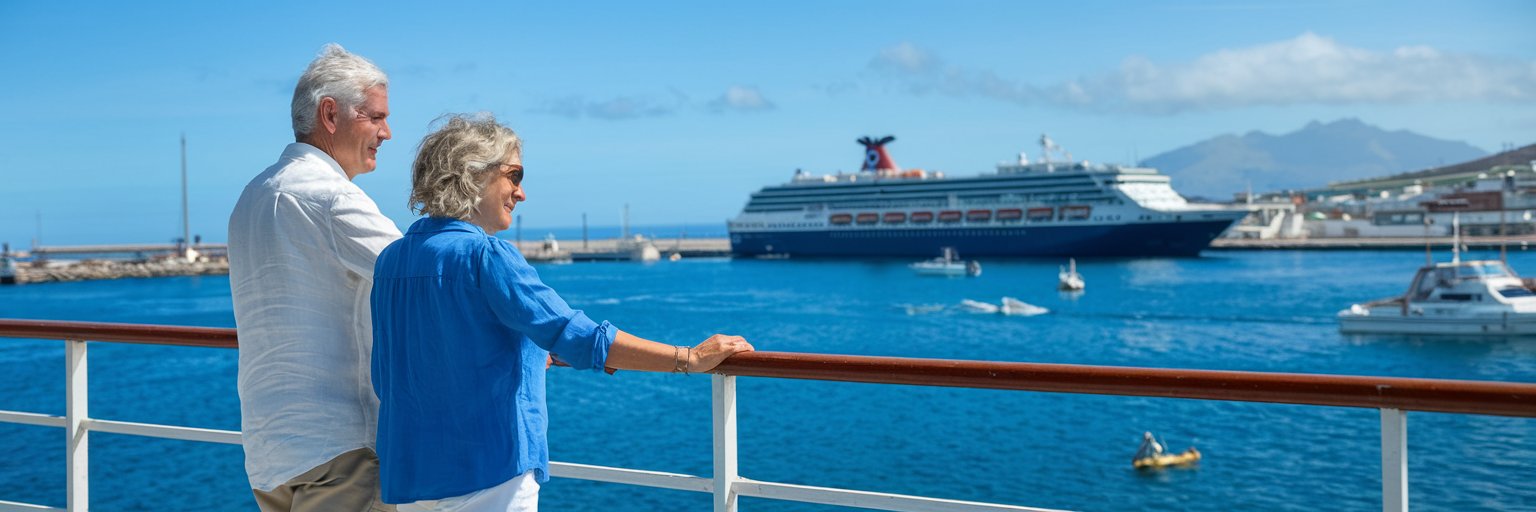 older couple casually dressed in shorts in Port of Gibraltar on a sunny day with a cruise ship in the background.