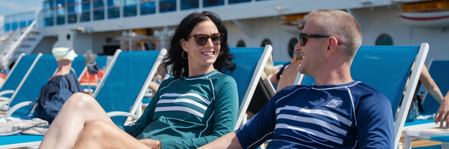 Mid aged lady and man on lounge chairs dressed in swimwear on a cruise ship. Sunny Day at Port of Southampton.