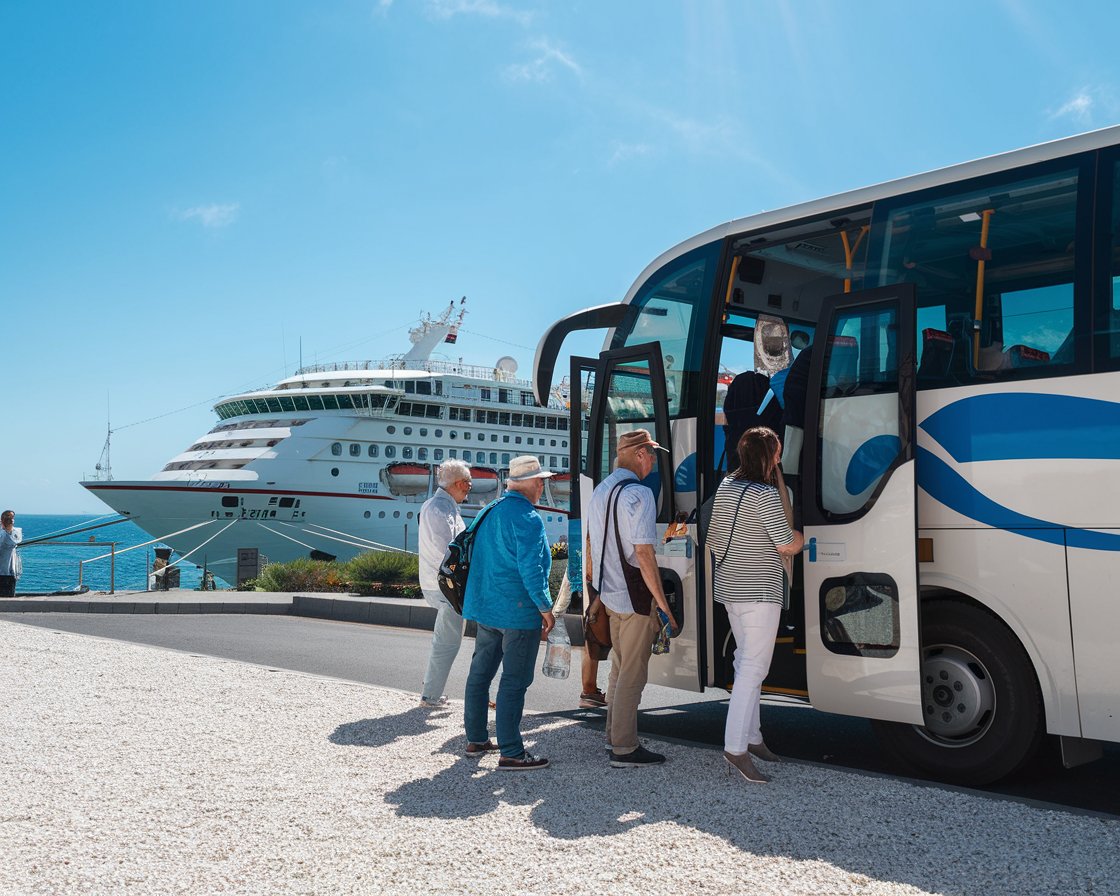 tourists boarding a bus with a cruise ship in the background