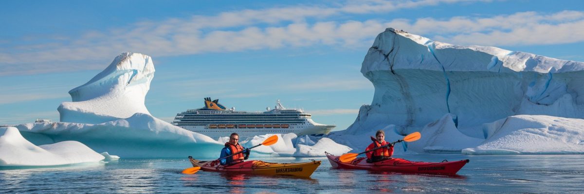 Kayakers near icebergs with a cruise ship in the background