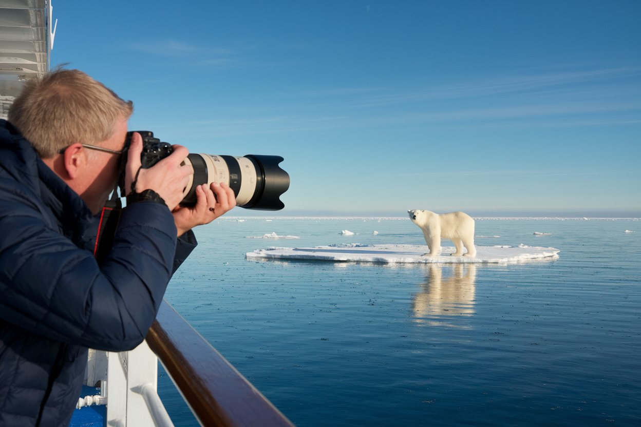 Man with a long zoom camera taking a photo of a polar bear from a cruise ship