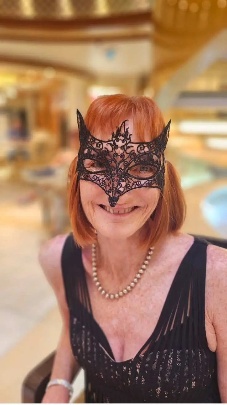 Author wearing black lace masquerade mask and pearl necklace with black dress at Cunard Queen Elizabeth masquerade ball