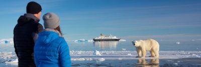 Two cruise guests looking at a polar bear in the Arctic