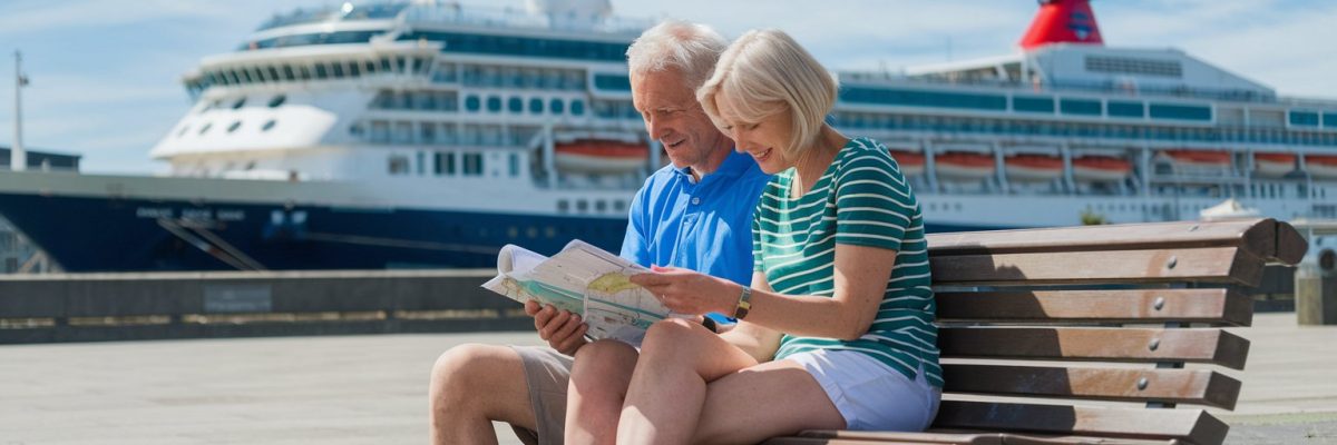 older couple sitting down, reading a map, casually dressed in shorts on a sunny day with a cruise ship in the background in Aberdeen, Scotland