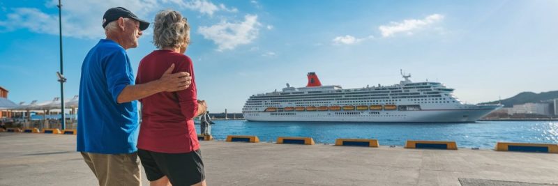 older couple casually dressed in shorts in Port of Palma de Mallorca on a sunny day with a cruise ship in the background.