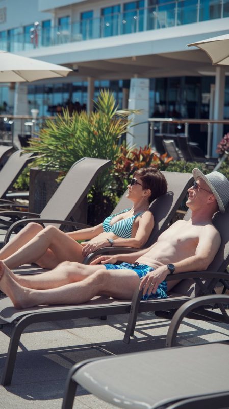 Mid aged lady and man on lounge chairs dressed in swimwear on a cruise ship on a sunny day at Monte Carlo Cruise Ship Port