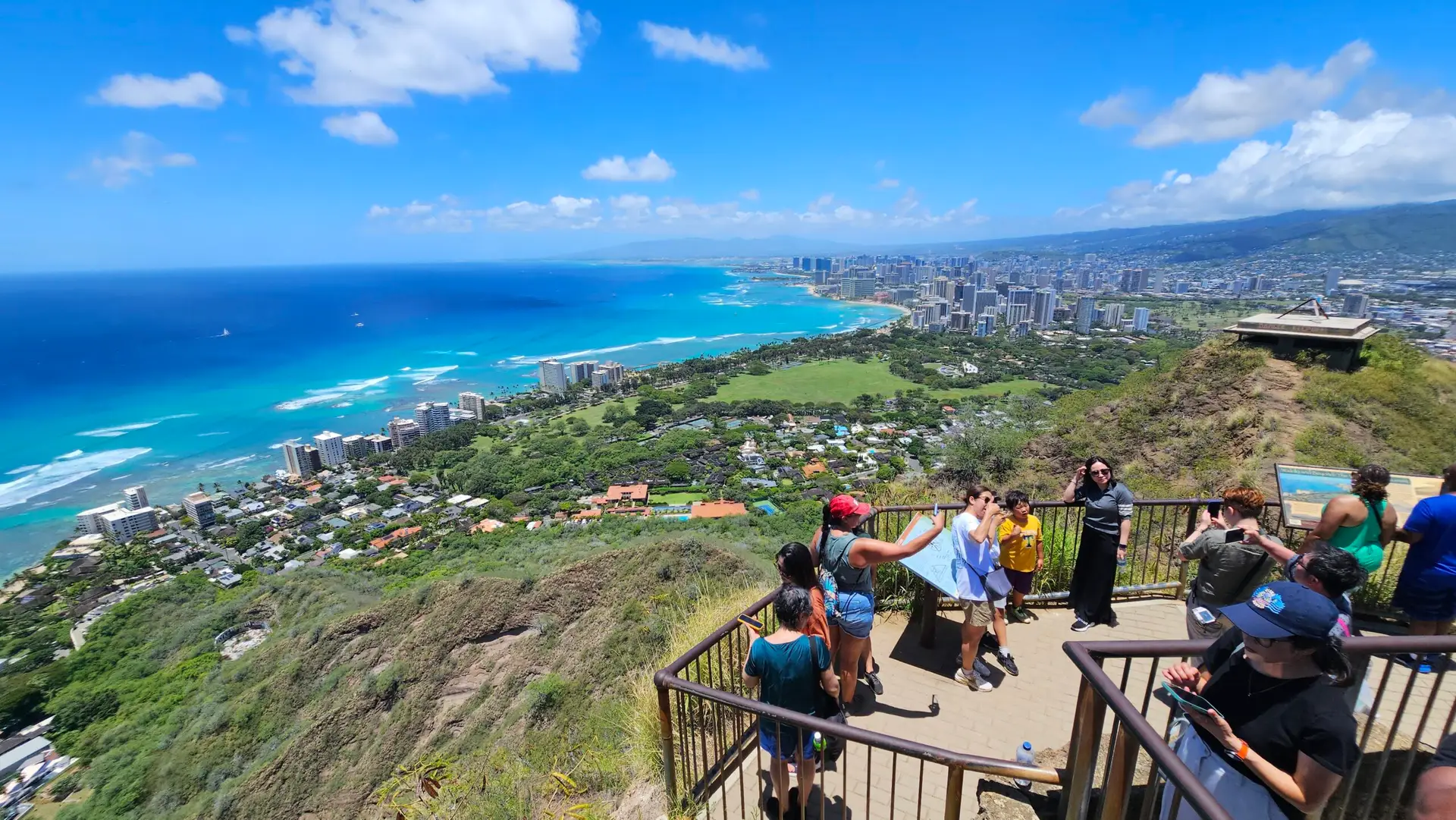 Diamond Head crater summit viewpoint showing panoramic view of Waikiki Beach, turquoise Pacific Ocean, and Honolulu skyline with cruise ship passengers at observation deck railing on Oahu