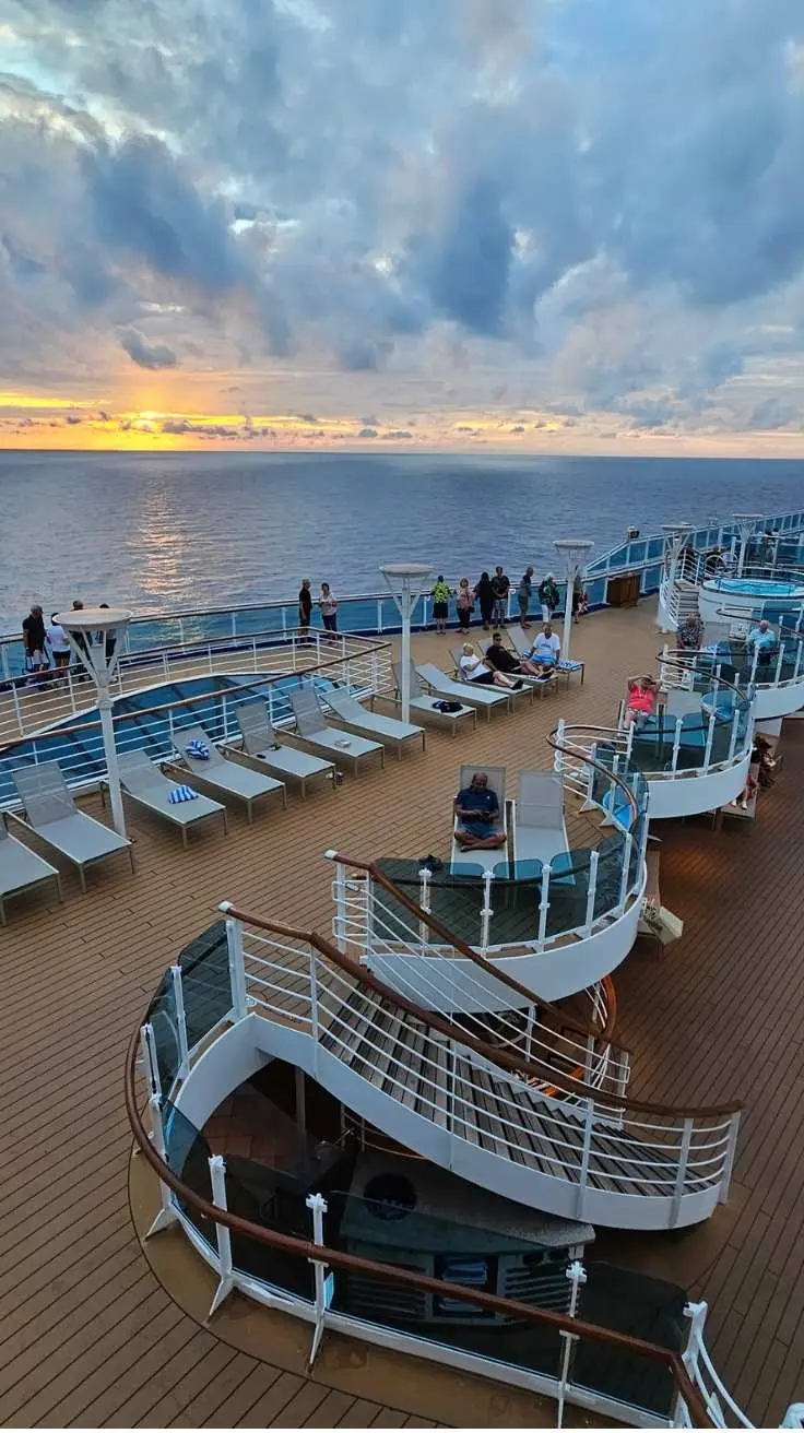 Royal Princess cruise ship pool deck at sunset with passengers in summer cruise-wear watching the ocean