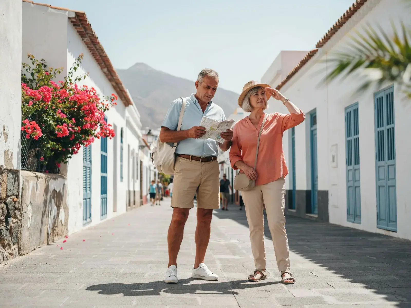Two travellers in their sixties reading a map on a whitewashed street in Santa Cruz de Tenerife, with Mount Teide behind.