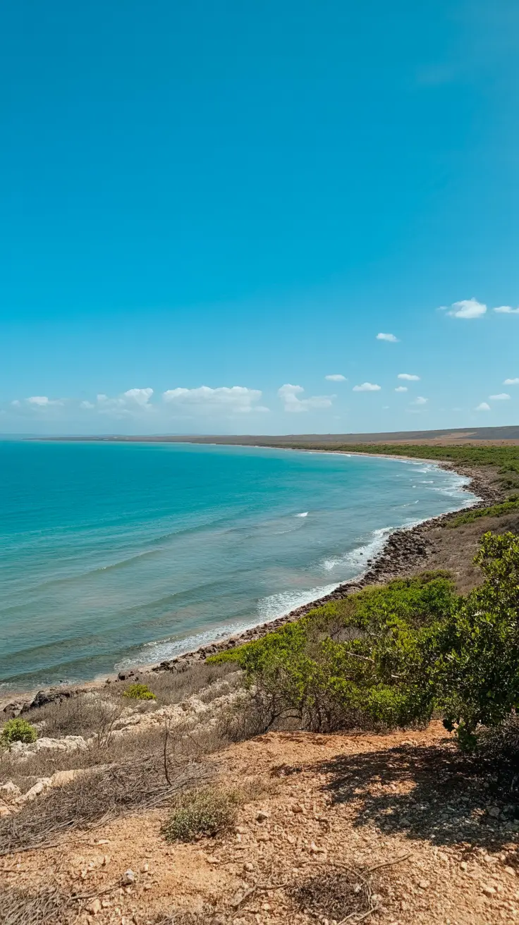 A high-resolution photograph of Cabo Rojo’s coastline on a bright, sunny day—clear blue skies, golden sunlight reflecting off calm turquoise waters, and dry, sunlit earth with sparse greenery, capturing the essence of its warm, dry climate.