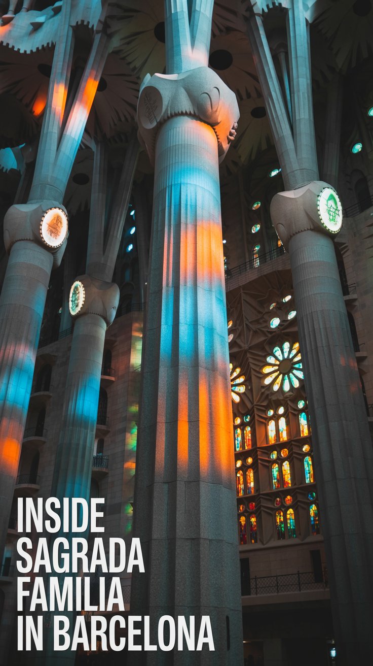 A photograph showcasing the interior of the Sagrada Familia basilica in Barcelona, focusing on a single soaring stone pillar. The pillar is intricately carved with branching patterns and illuminated by shafts of sunlight filtering through the stained-glass windows, casting vibrant hues of blue and red across the stone. In the bottom left corner, large text is aligned to the left reading "Inside Sagrada Familia in Barcelona". The scene is captured with a wide-angle lens, emphasizing the scale and grandeur of the architectural space.