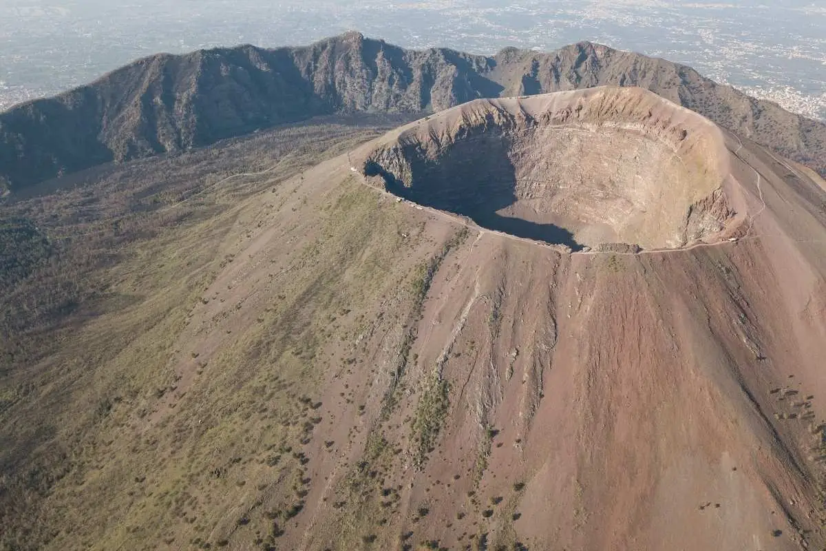Aerial view of Mount Vesuvius crater showing volcanic cone, inner crater depression, hiking trail along rim, and surrounding Monte Somma caldera