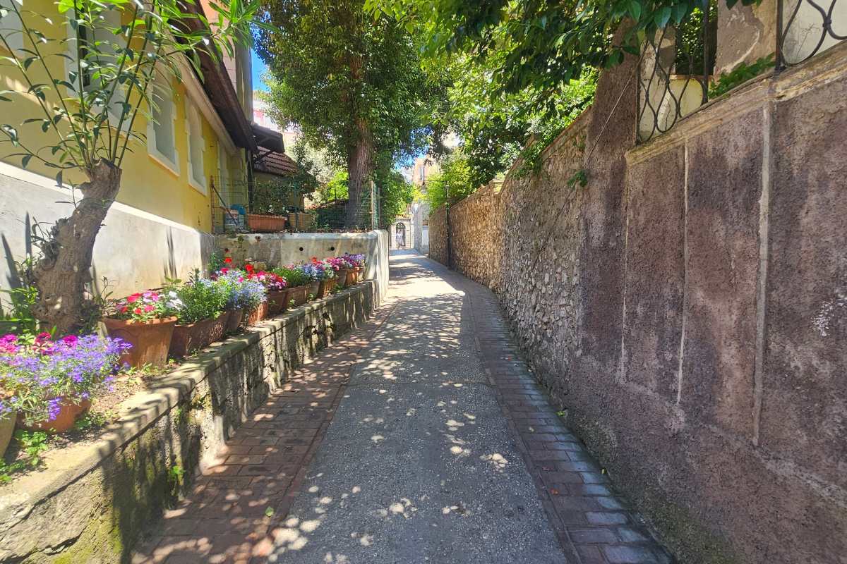 Peaceful narrow lane in Anacapri with colorful flower pots, traditional yellow villa, and dappled tree shade