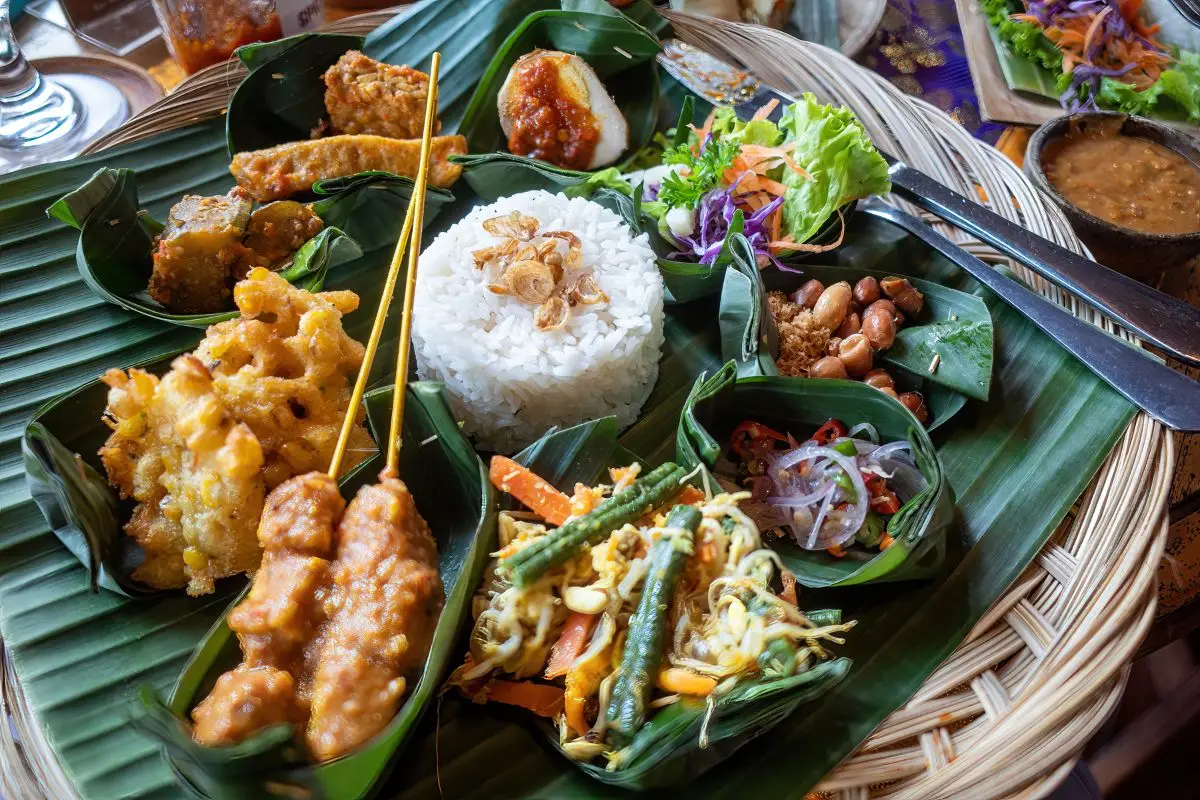 Traditional Balinese food platter on banana leaf with rice satay vegetables and multiple small dishes