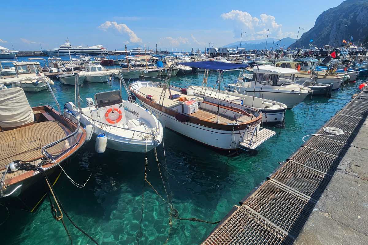 Marina Grande harbor in Capri with luxury yachts and fishing boats moored in crystal-clear turquoise water with dramatic cliffs behind