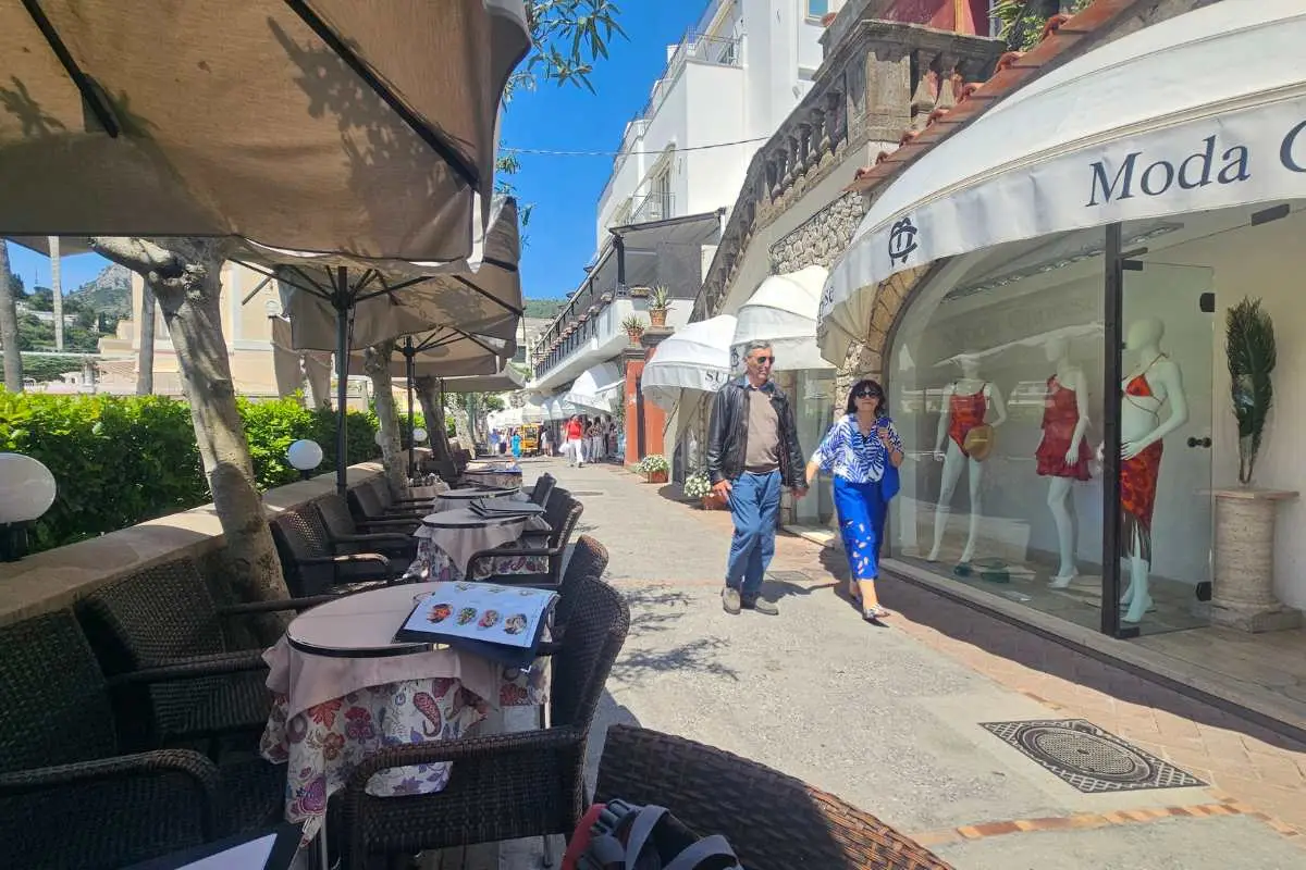 Upscale shopping street in Capri town with designer boutiques, outdoor cafes, and tourists browsing luxury fashion stores