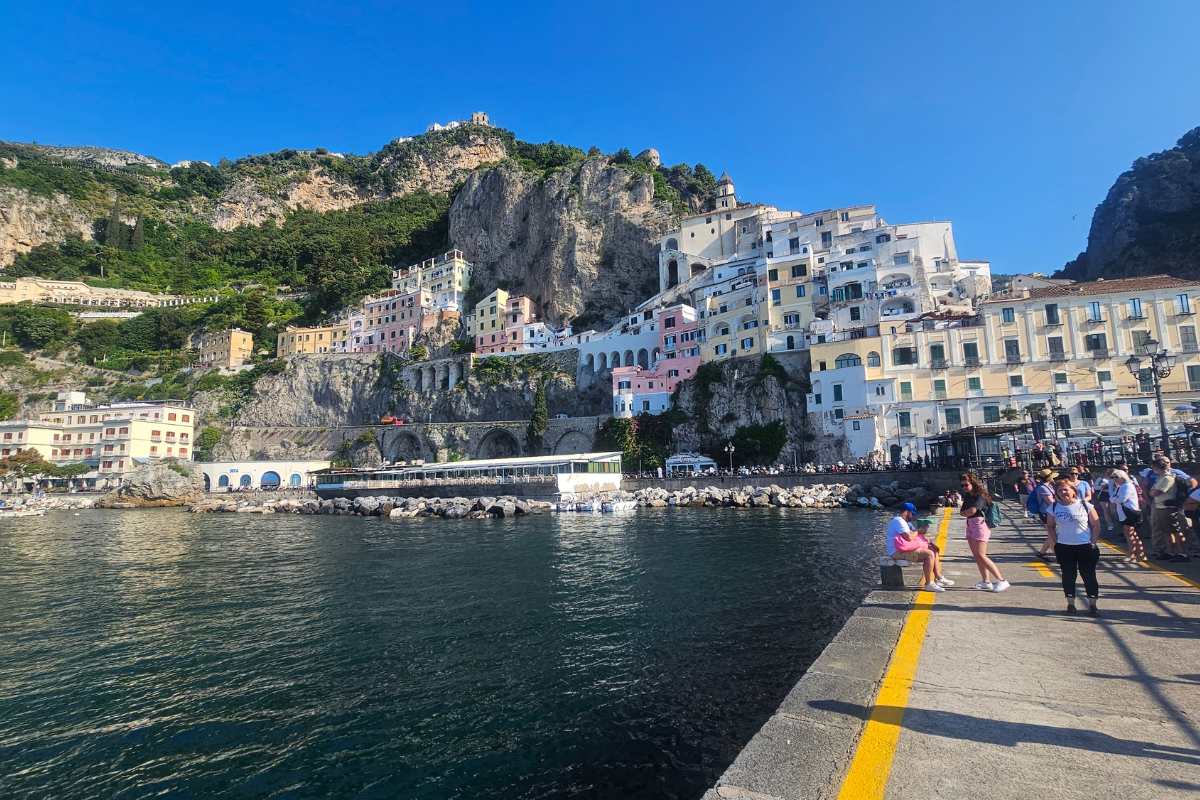 Capri viewed from ferry showing pastel-colored buildings stacked on cliffsides with tourists on ferry dock