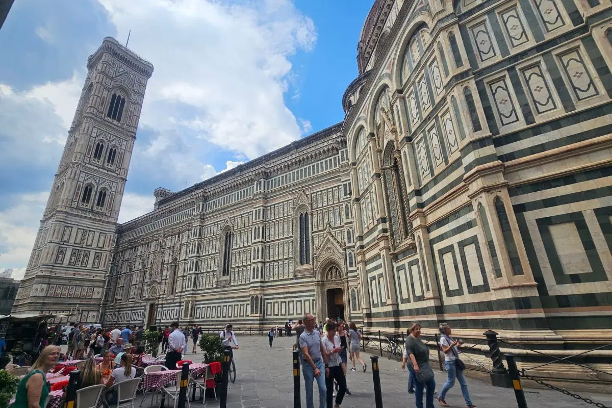 Florence Cathedral Duomo with distinctive green and white marble exterior and Giotto's Bell Tower with tourists in the square