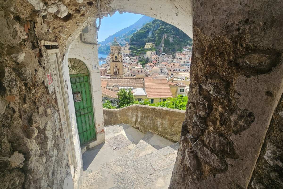 Stone archway framing scenic view of Positano's colorful buildings and church dome cascading down cliffsides to the Tyrrhenian Sea on Italy's Amalfi Coast