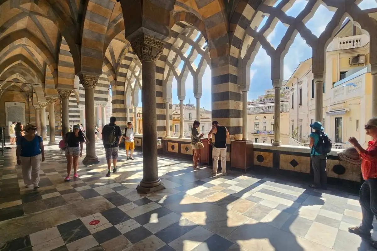 Interior courtyard of Positano church showing distinctive striped columns and vaulted arches with tourists exploring the medieval architecture