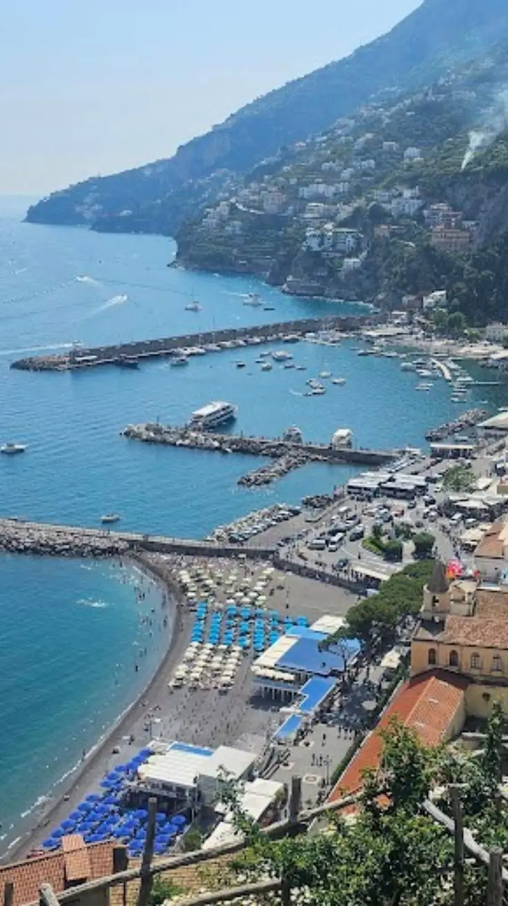 Aerial view of Amalfi harbour, ferry pier, beach and town rooftops from the hillside above