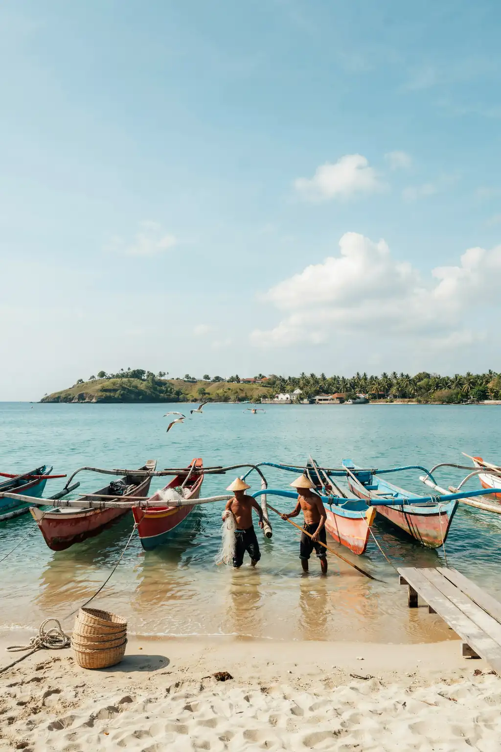 Traditional wooden boats moored in a Bali harbour with coastline and hills in the background on a sunny day