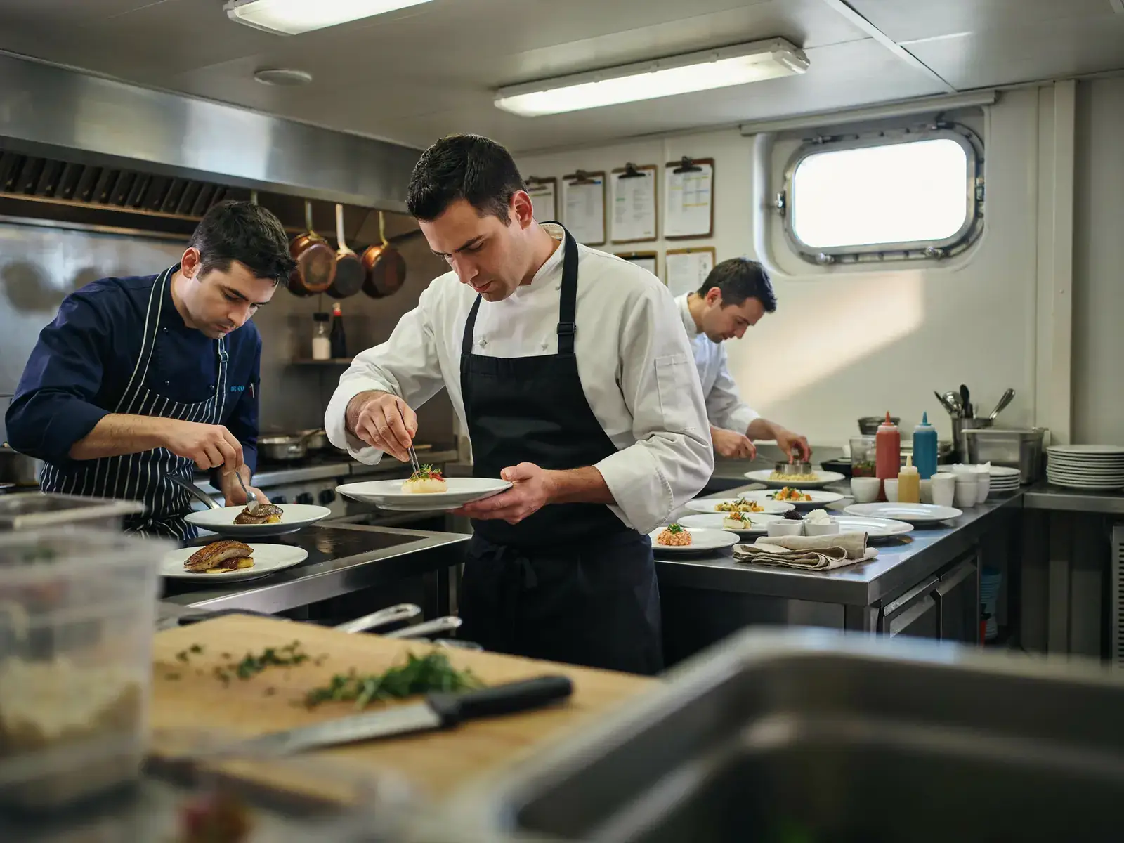 Chefs plating gourmet dishes in a cruise ship galley kitchen