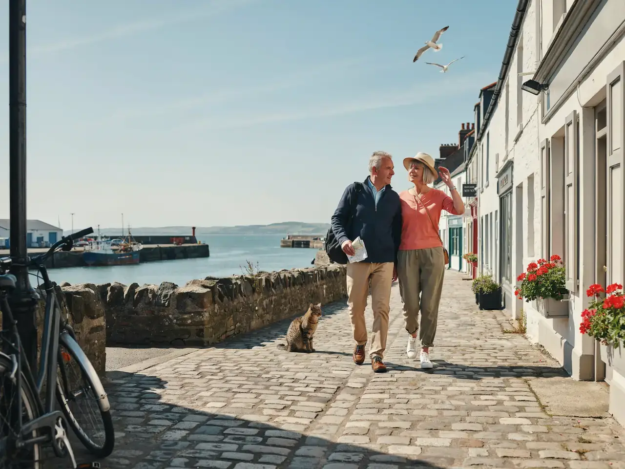 Two older tourists walking side by side in bright sunshine, dressed casually