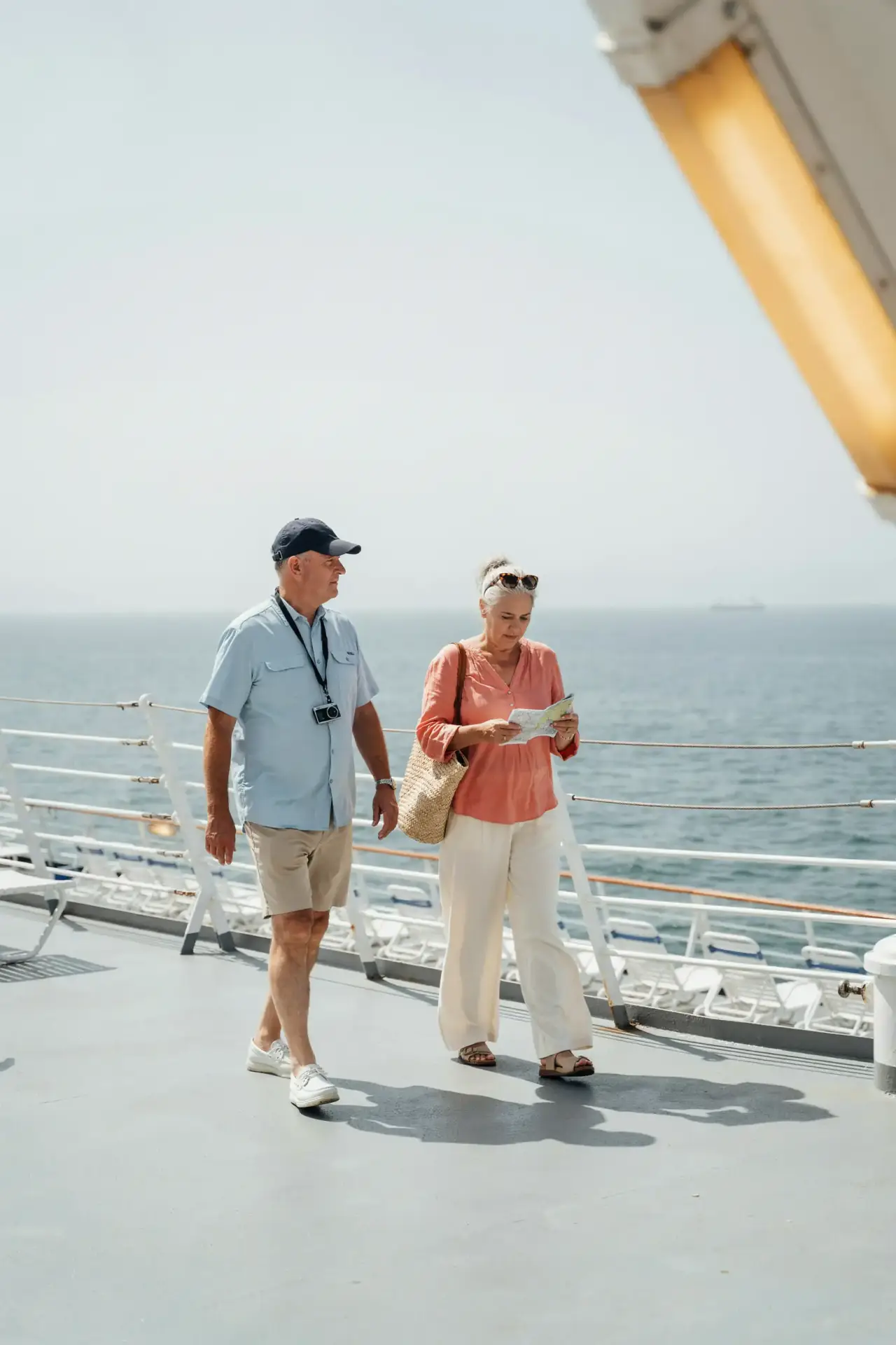 A group of older tourists walking together in the sunshine on a ship's outdoor deck