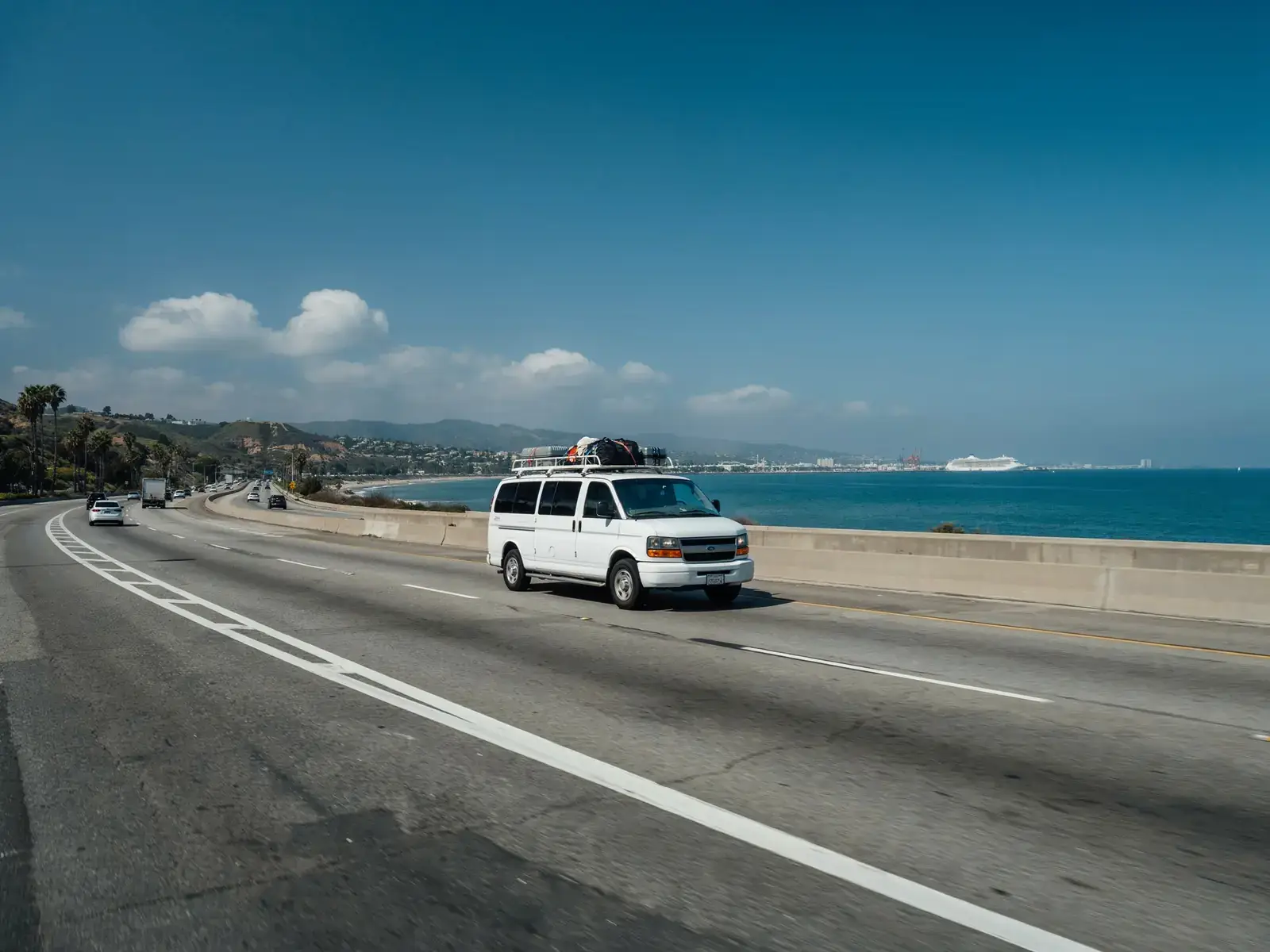 A shuttle vehicle travelling along a roadway connecting LAX airport to the Los Angeles cruise port on a sunny day.