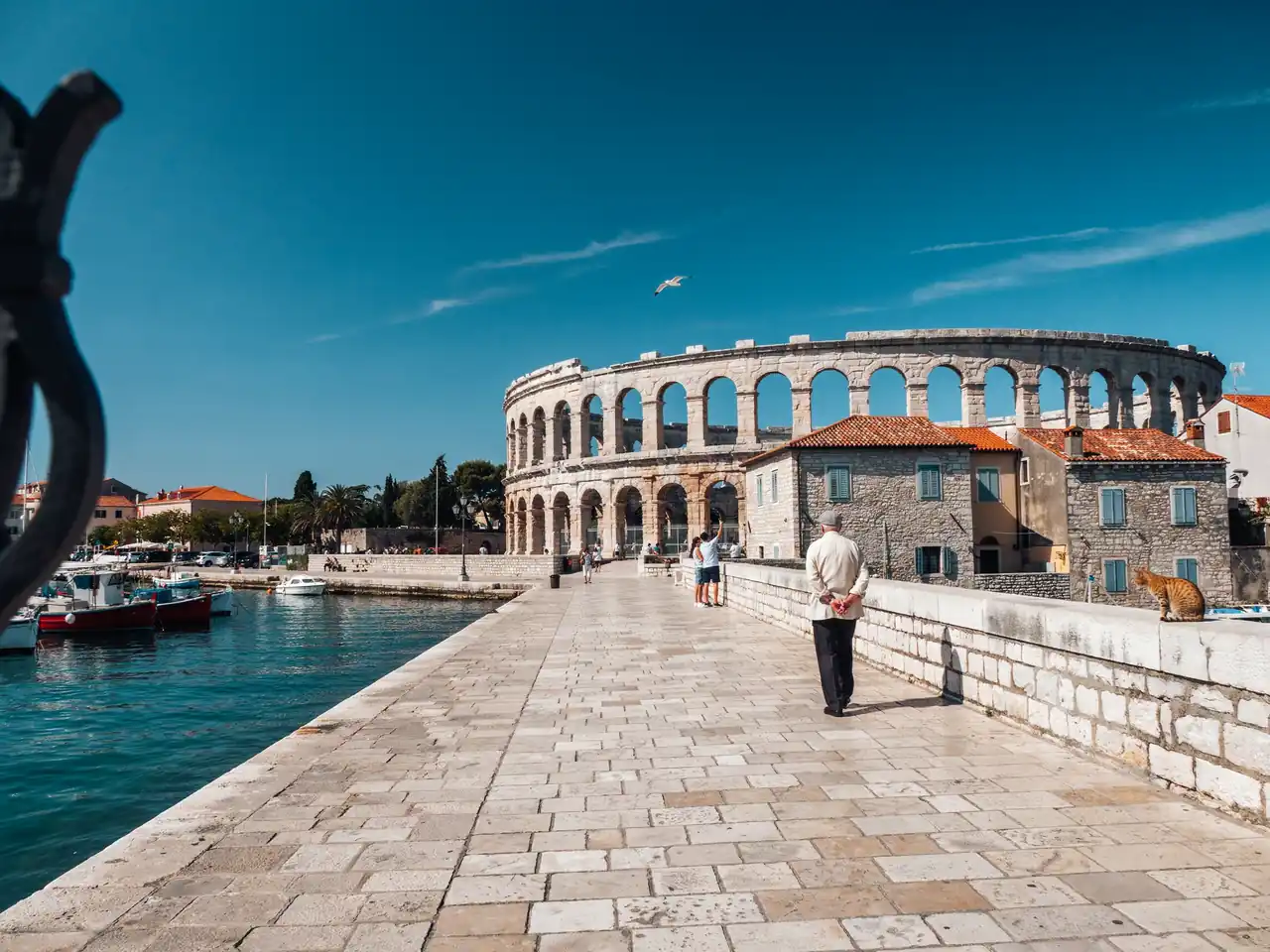 A sunny walking route in Pula leading from the harbour quay towards the ancient Roman arena in the distance.