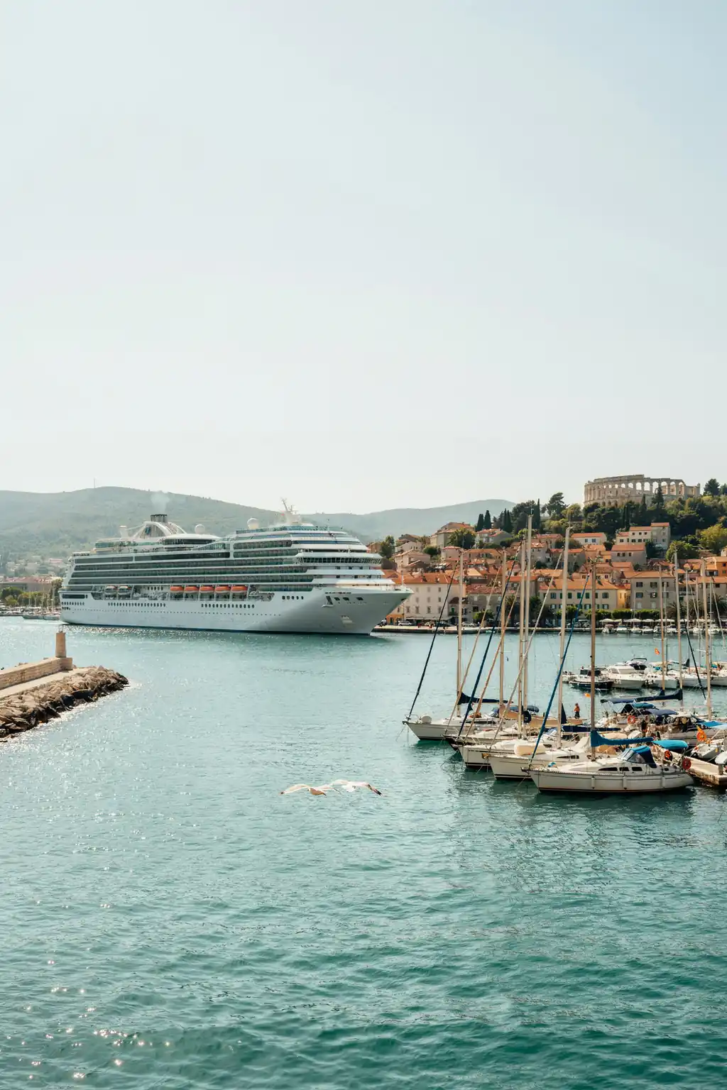 Cruise ship docked in Pula harbour with coastal skyline in the background on a sunny day