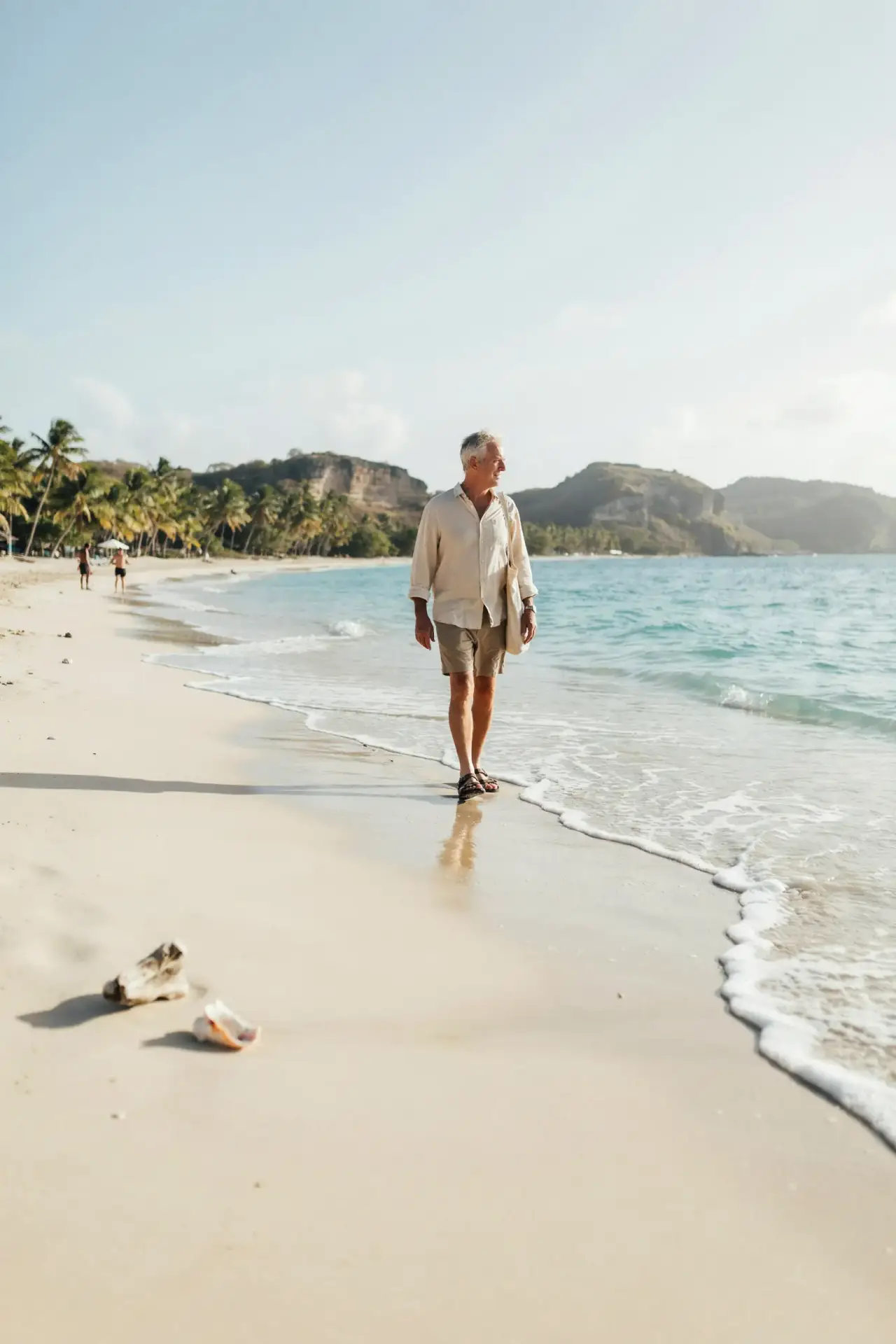 A group of older tourists relaxing and walking along a sunny stretch of golden sand beside calm turquoise water, with green hills in the distance
