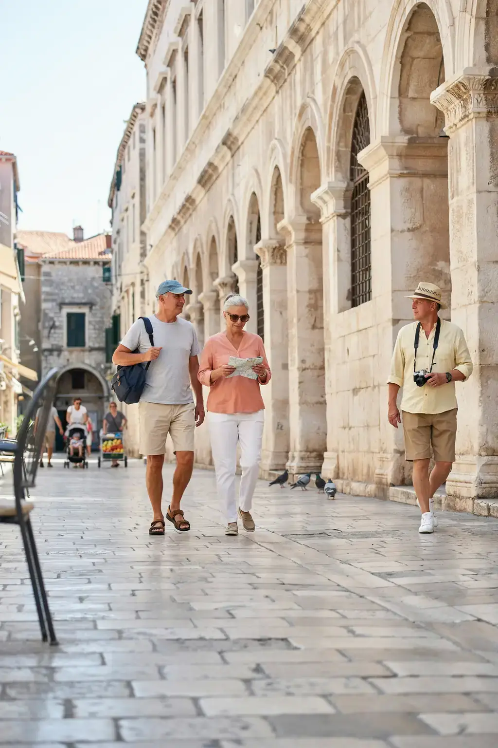 A group of older tourists walking together on a sunlit stone street lined with historic buildings