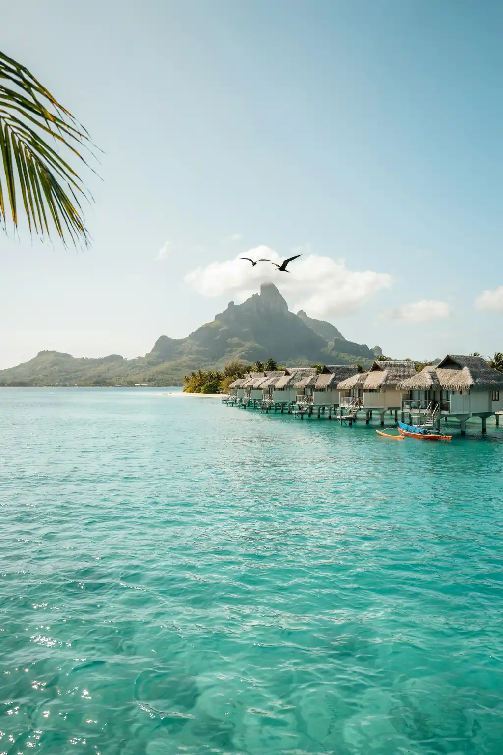 Turquoise lagoon in Bora Bora with overwater bungalows and green mountain peak in the background