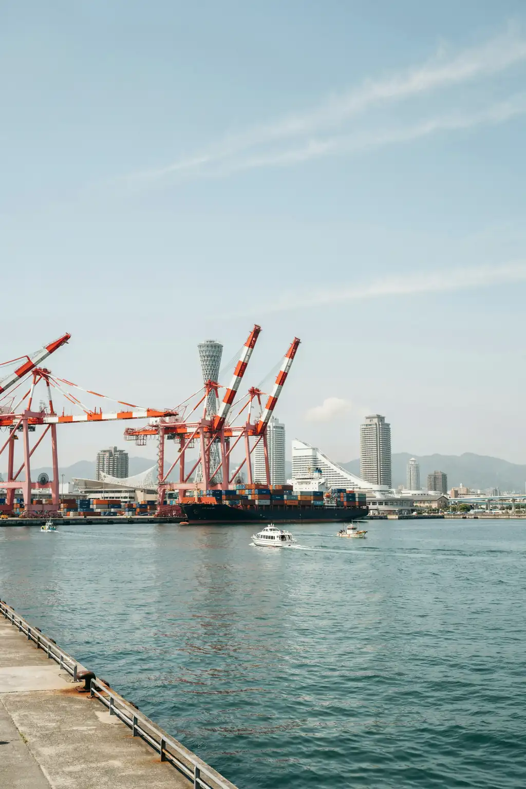 Kobe harbourfront skyline with port cranes and boats on a sunny day