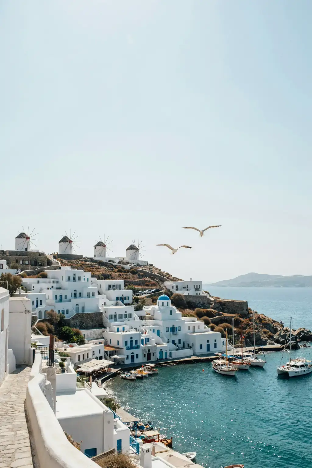 Mykonos harbour lined with whitewashed buildings and traditional windmills on a hillside