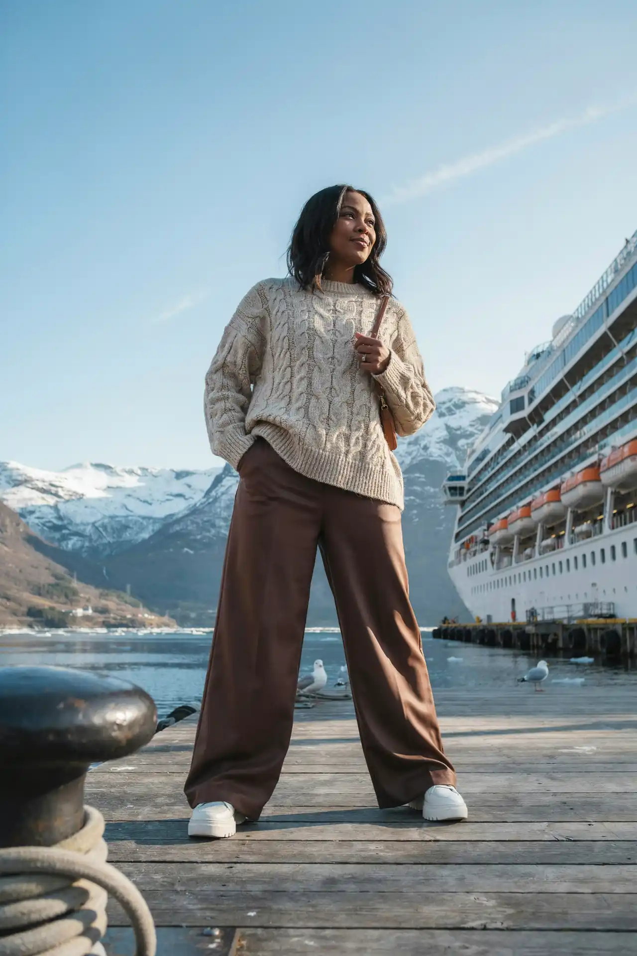 Black woman in a cream cable knit jumper and chocolate wide-leg trousers boarding an Alaska cruise ship