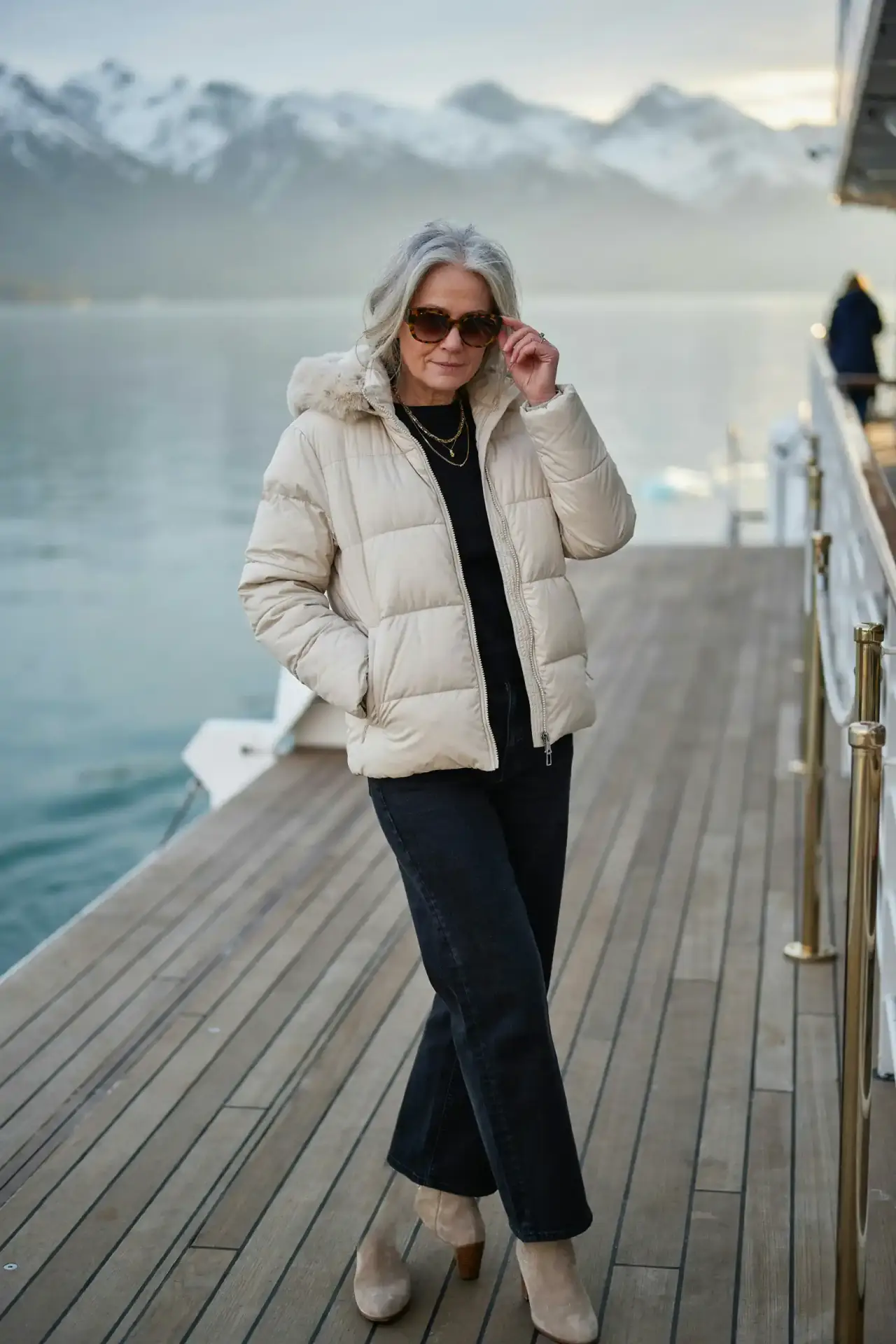 Woman in her 60s in a cream puffer jacket with a faux fur hood and wide-leg jeans at sail-away in Alaska
