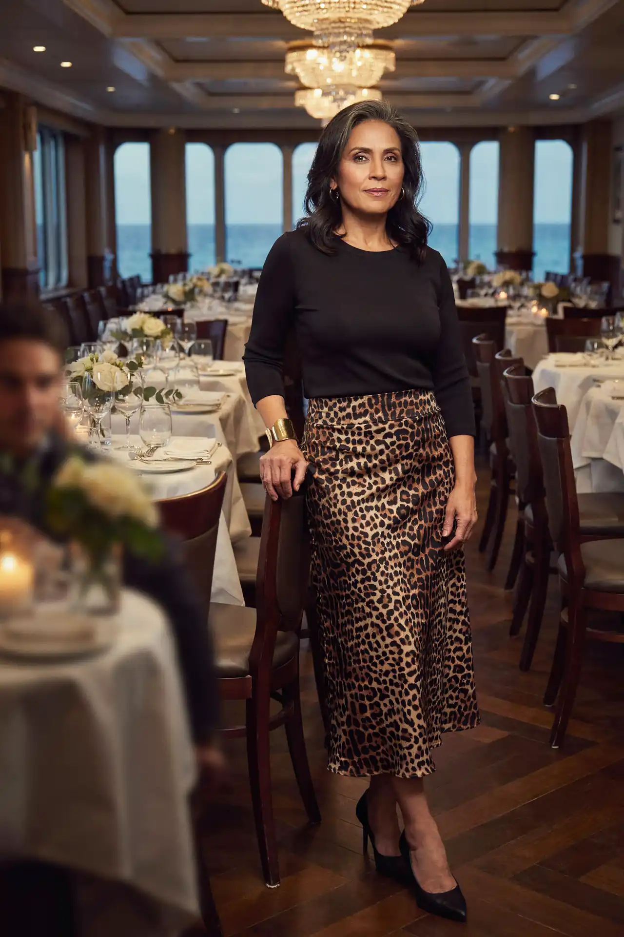 Latina woman in a leopard print satin midi skirt and black fitted top in a cruise ship dining room