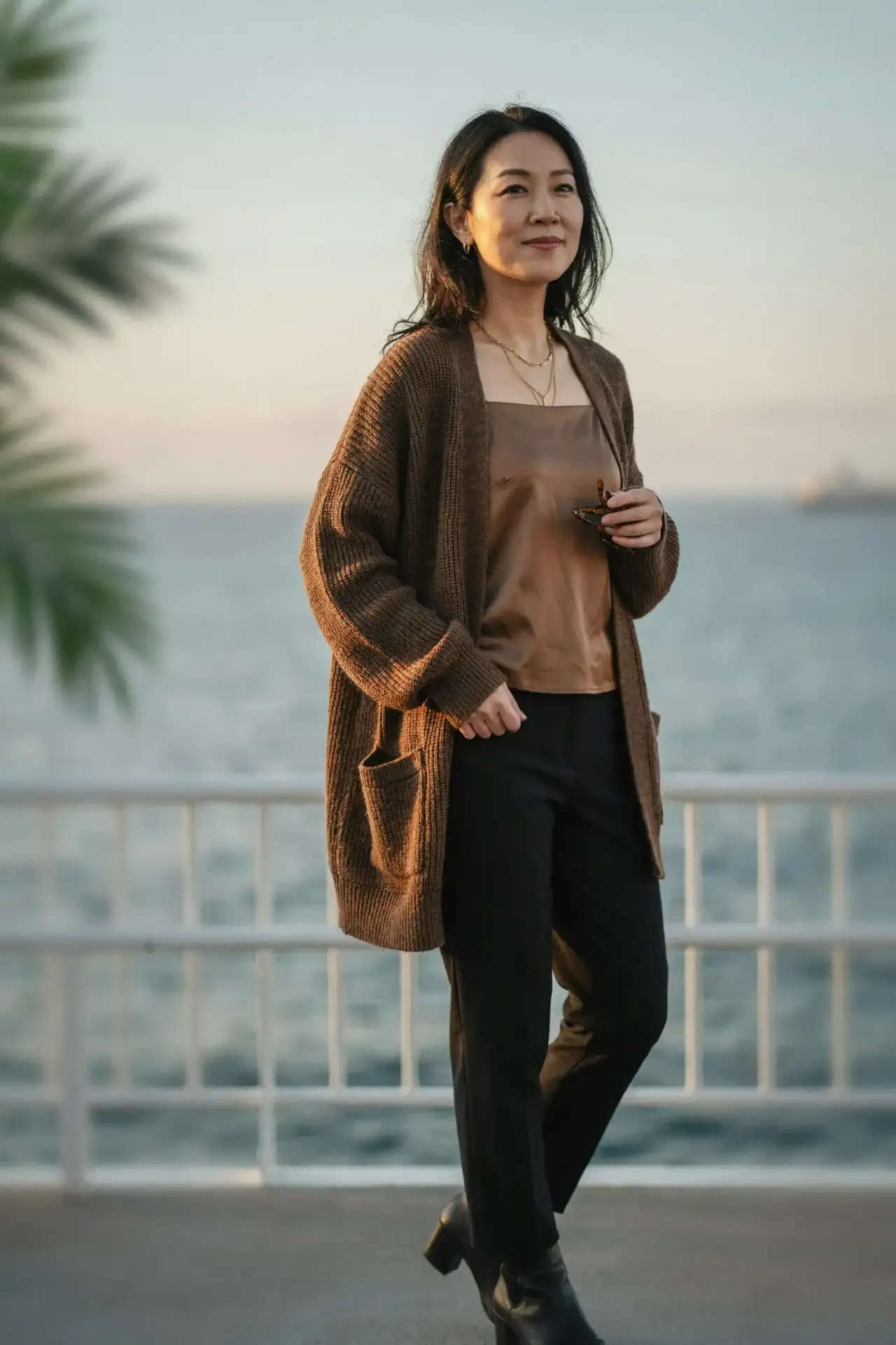 Asian woman in a brown oversized cardigan over a bronze satin cami on an Alaska cruise deck
