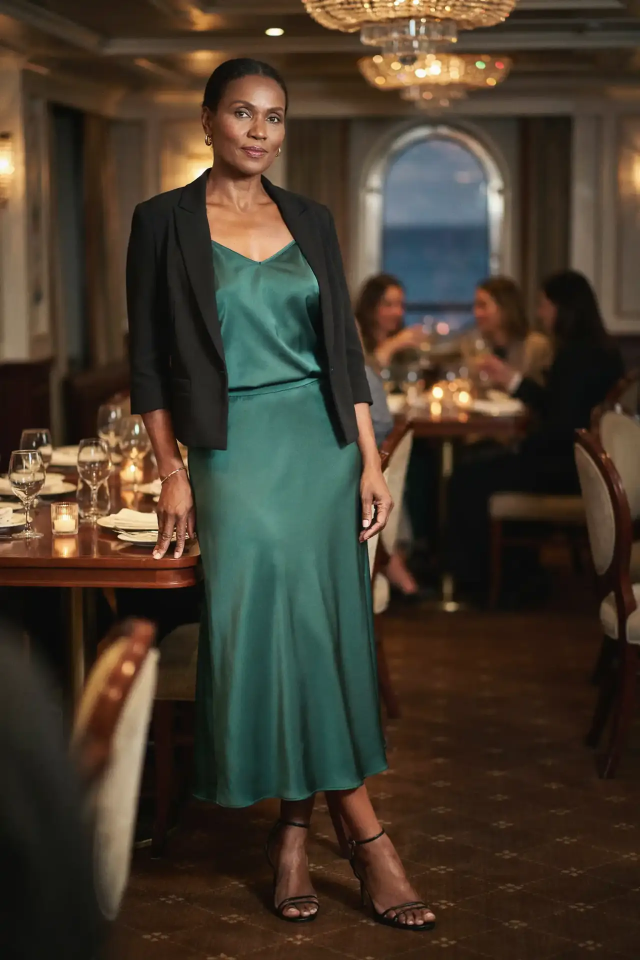 Black woman in an emerald satin co-ord and black cropped blazer in a cruise ship dining room