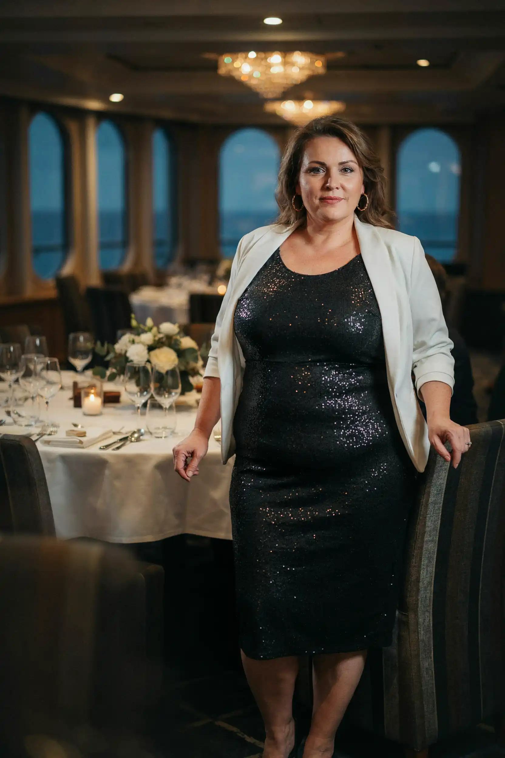Plus-size woman in a black sequin midi dress with a white blazer on an Alaska cruise formal night