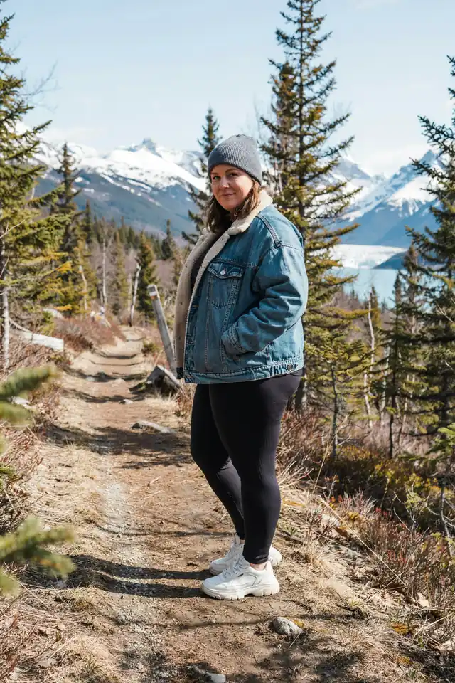 Plus-size woman in a sherpa-lined denim jacket and black leggings on an Alaska excursion
